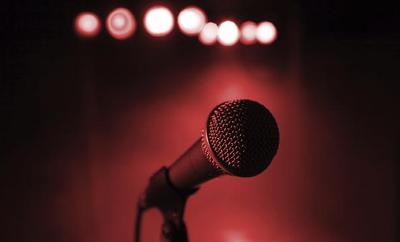 Image Description: [Photo of a vacant microphone on a stage illuminated by red lights]